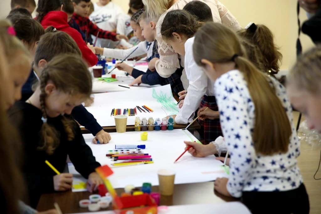 Children making art with paints and paper at tables