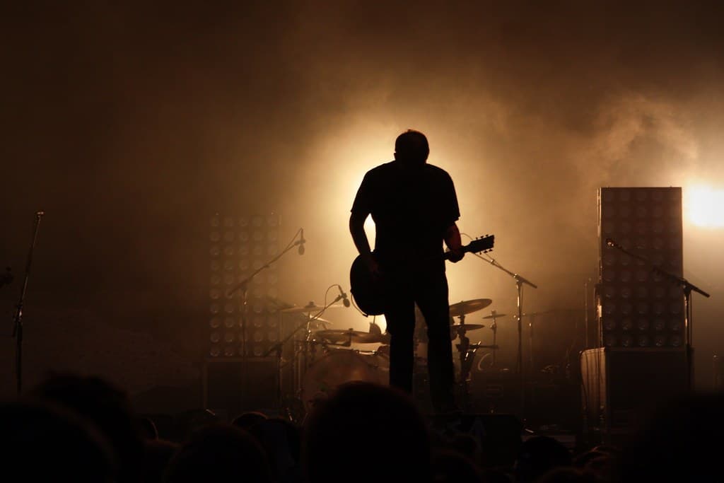 A solo musician silhouetted with a guitar on a smoky stage